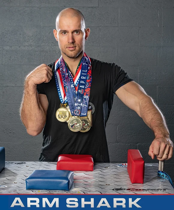 Andrei Sharkevich at an armwrestling table wearing his championship medals